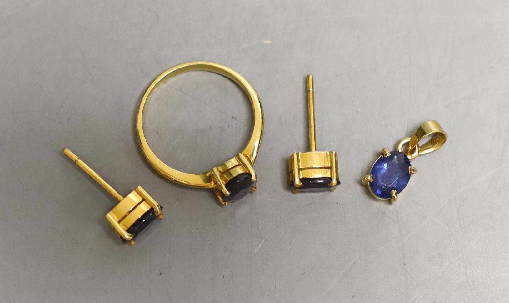A modern suite of yellow metal and synthetic? sapphire set jewellery, comprising a ring, pendant and pair of earrings, the ring and pendant stamped 18k, gross 7.5 grams.